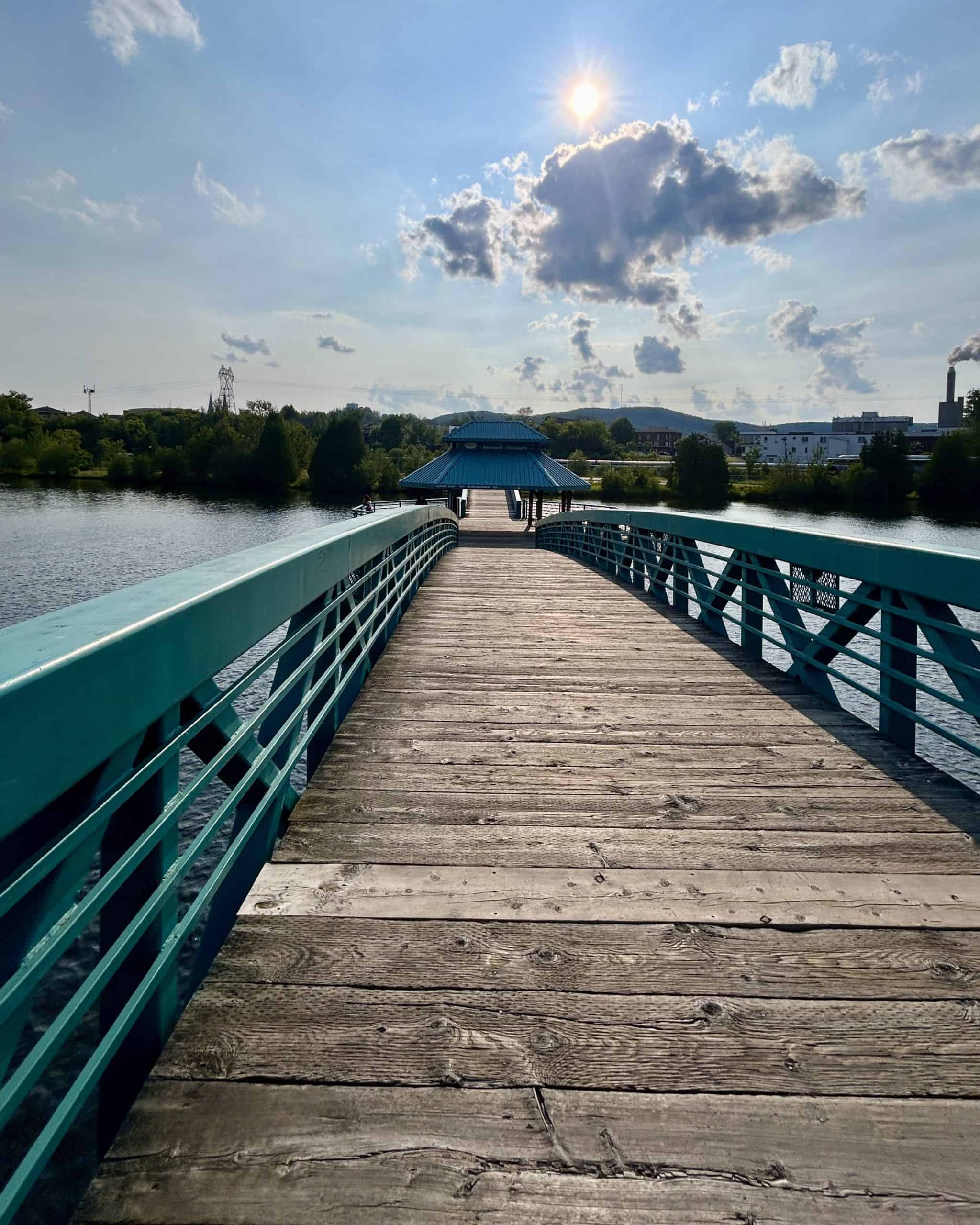This scenic riverside boardwalk in Edmundston, New Brunswick, offers a serene spot to walk, relax, and enjoy the town's blend of nature and architecture. Surrounded by lush greenery, the walkway overlooks calm river waters with charming local houses and the skyline of Edmundston in the background. Even under moody clouds, the view feels peaceful and welcoming — a must-visit spot when exploring Edmundston on your RV adventure.