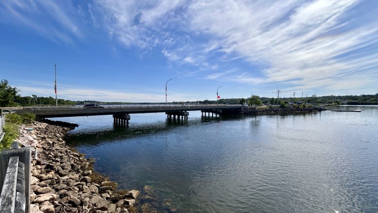 Bridge with Canadian flags spanning calm waters of Bathurst Basin in New Brunswick, ideal for scenic RV travel routes.